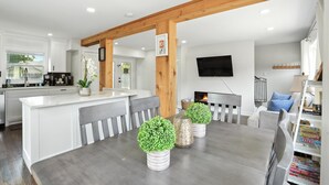 Una cocina moderna con armarios blancos, una viga de techo de madera y un comedor con mesa y sillas.