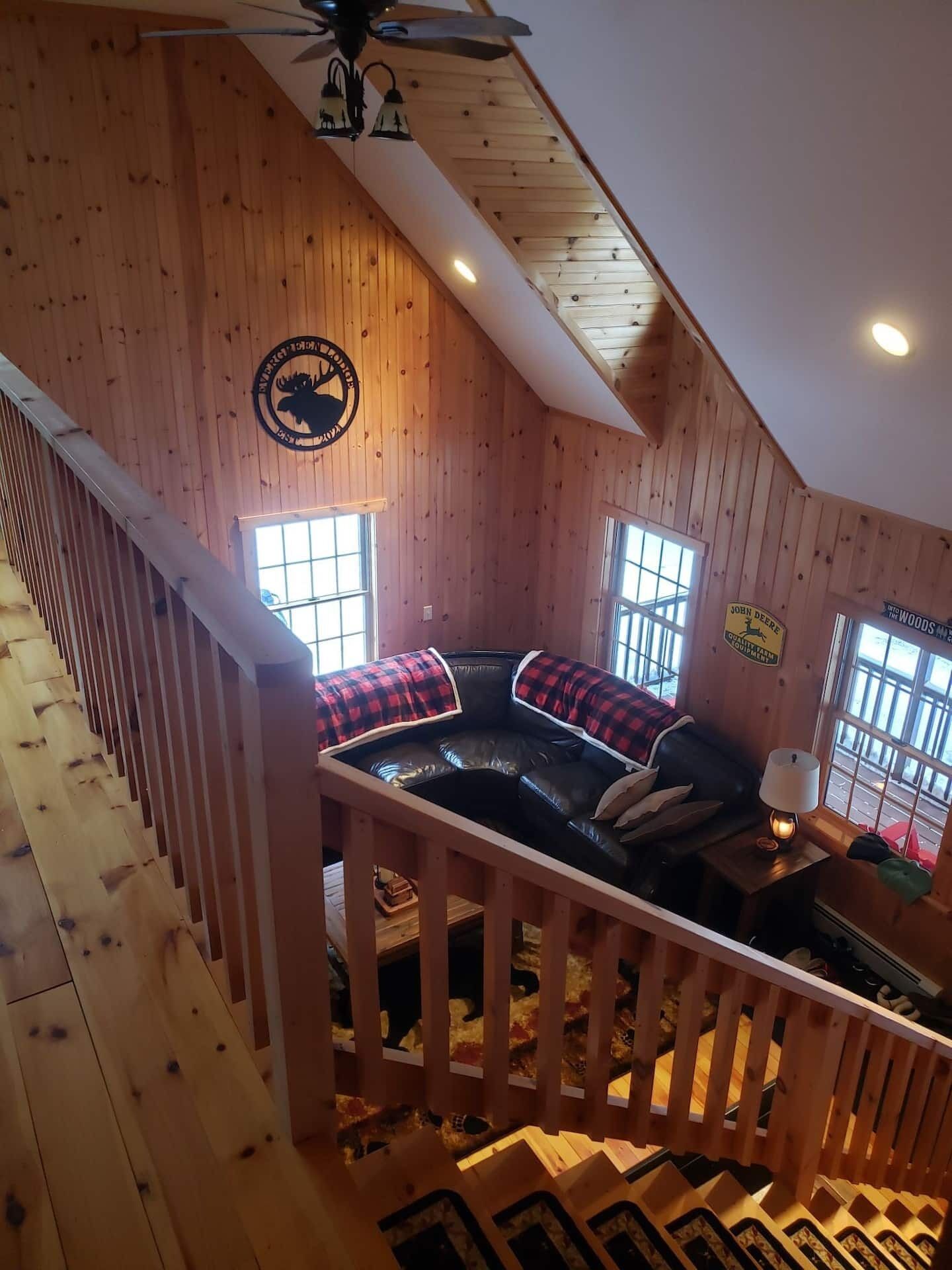 Ein gemütliches Blockhaus-Interieur mit einer erhöhten Sitzgruppe, Holzwänden und einem Deckenventilator.