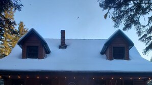 Uma cabana com lareira na neve, rodeada por cadeiras vermelhas.