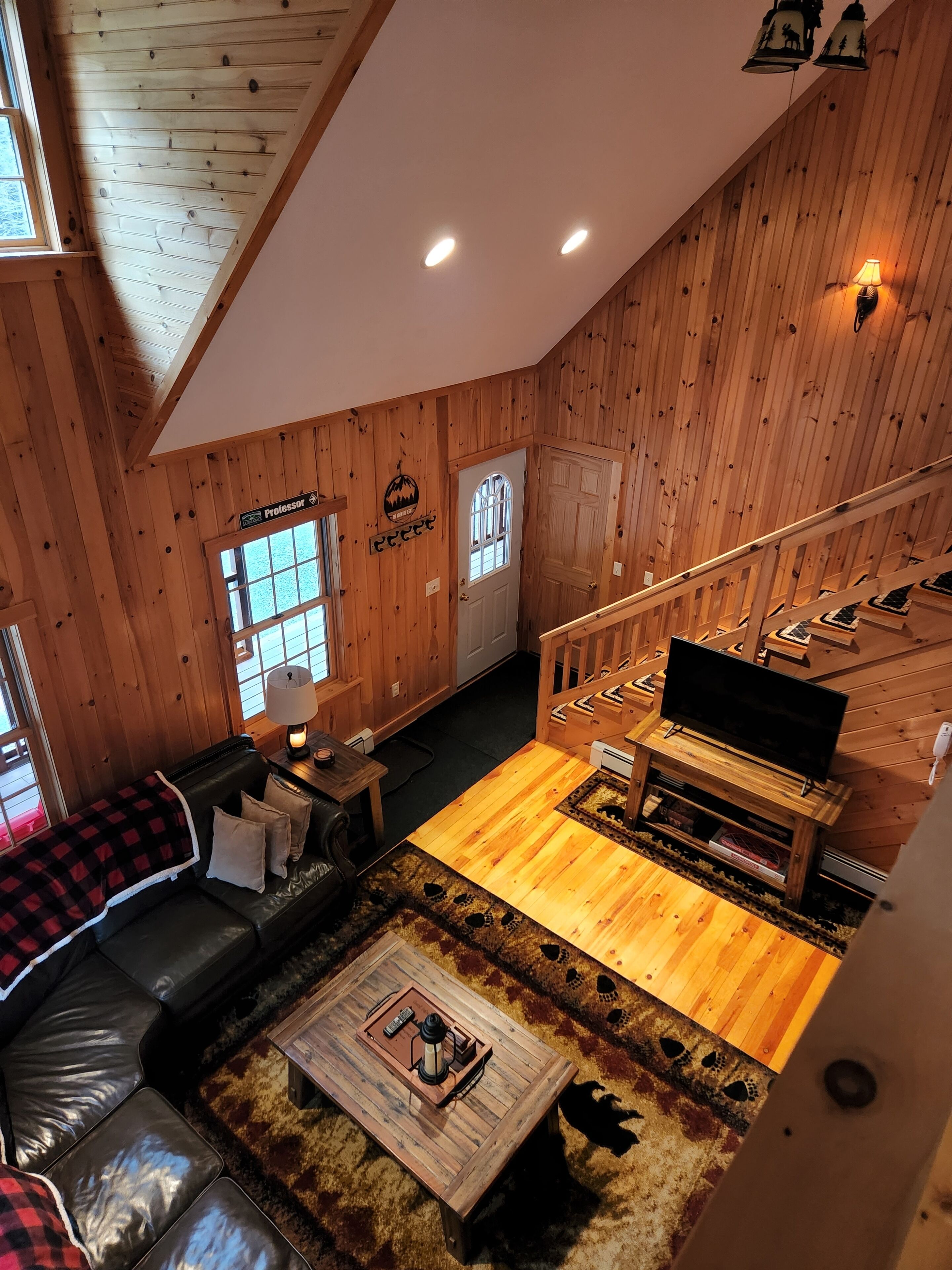 L’intérieur chaleureux d’un chalet, avec un revêtement mural en bois, un escalier, un salon doté d’un canapé et d’une table basse, et un téléviseur.