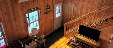 L’intérieur chaleureux d’un chalet, avec un revêtement mural en bois, un escalier, un salon doté d’un canapé et d’une table basse, et un téléviseur.