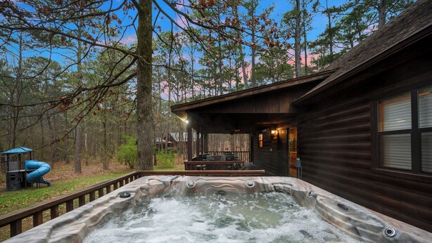 A hot tub in a wooded area with a wooden cabin in the background.