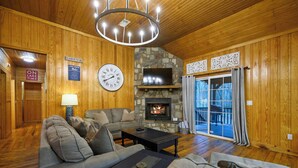 A wooden interior with a stone fireplace, a sofa, a coffee table, and a clock on the wall.