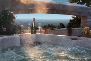 Ein Whirlpool mit einer Champagnerflasche und einem Glas, umgeben von Blumen und Blick auf die Landschaft.