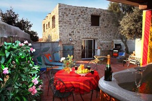 Eine Terrasse im Freien mit einem Steinhaus im Hintergrund, einem Tisch mit rotem Tischläufer und einer Fontäne.