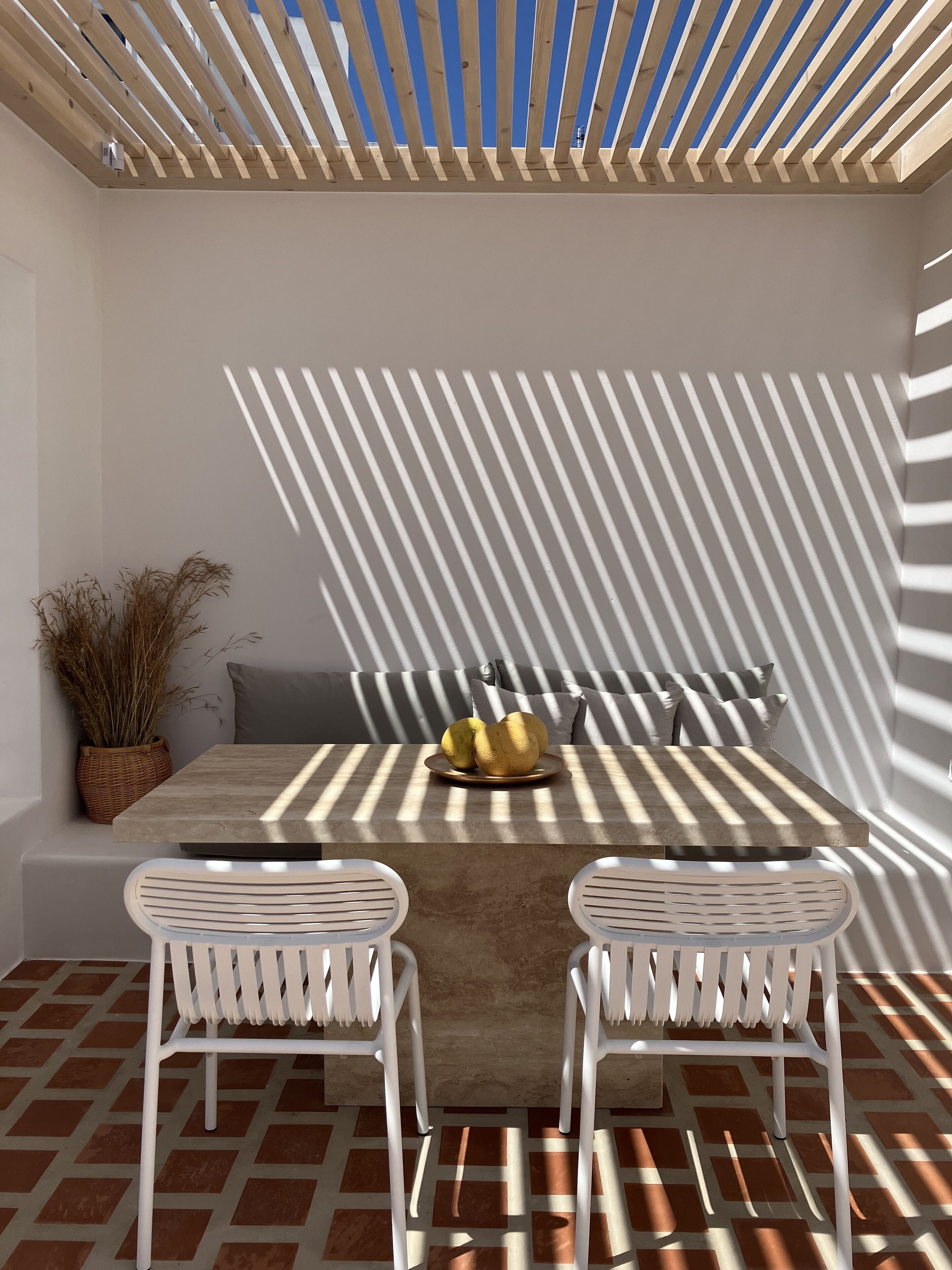 Un espacio moderno para comer al aire libre con una mesa de hormigón, dos sillas blancas y una estructura de techo de madera.