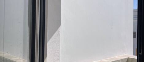 A window view of a swimming pool with a tiled edge, a white wall, and a clear blue sky.