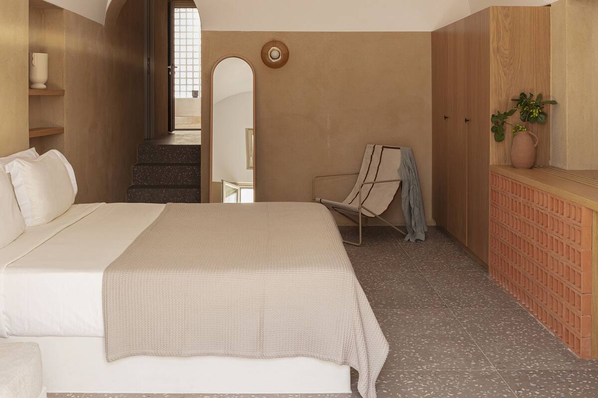 Ein Schlafzimmer mit einem großen Bett, einem Sessel, einem kleinen Tisch und einer Topfpflanze.