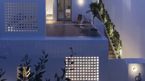 A modern building with a balcony, a staircase, and a lit-up logo. - Ethos Vegan Suites (Santorini)
