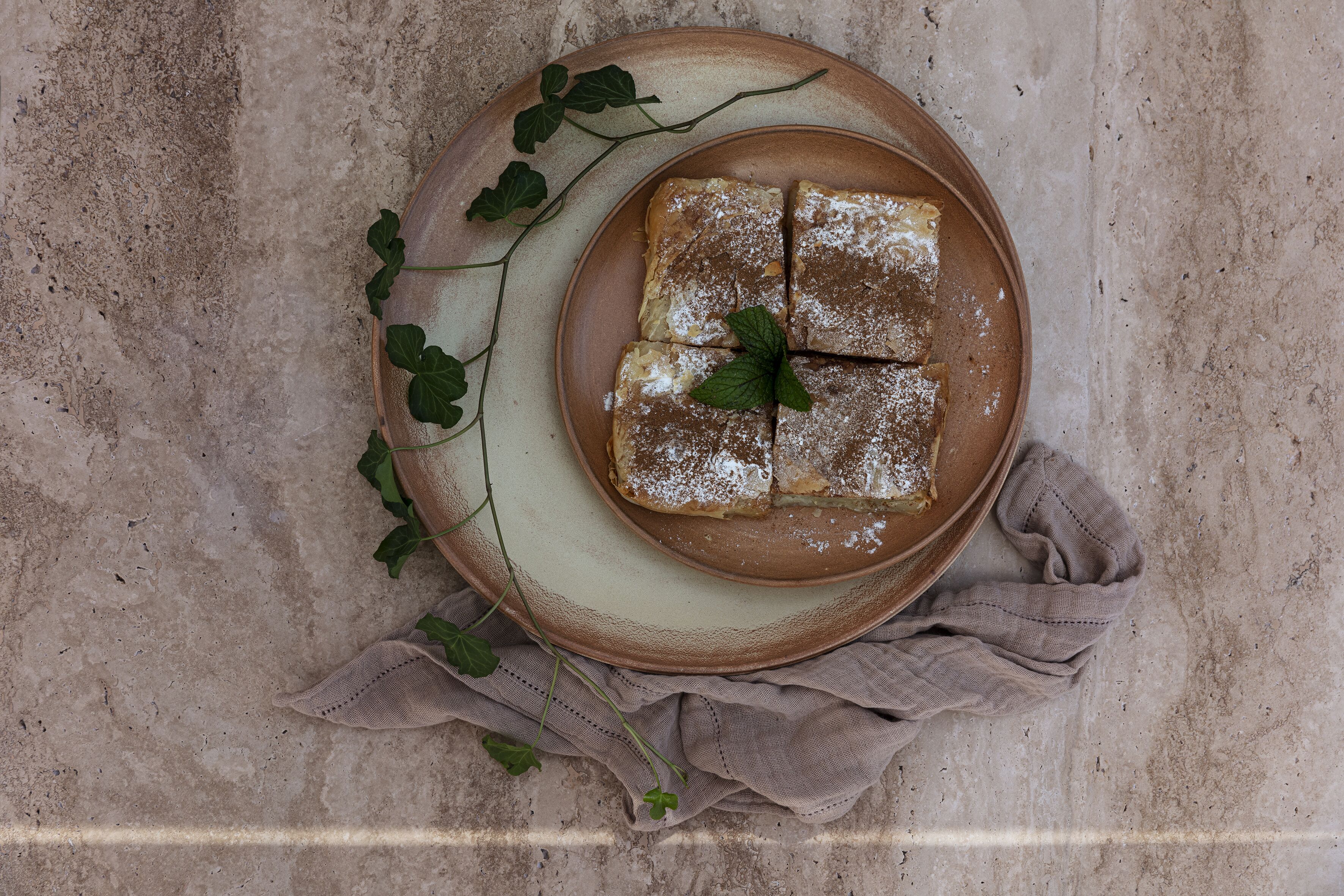 A plate of sliced bread with powdered sugar and a mint leaf on a textured surface.
