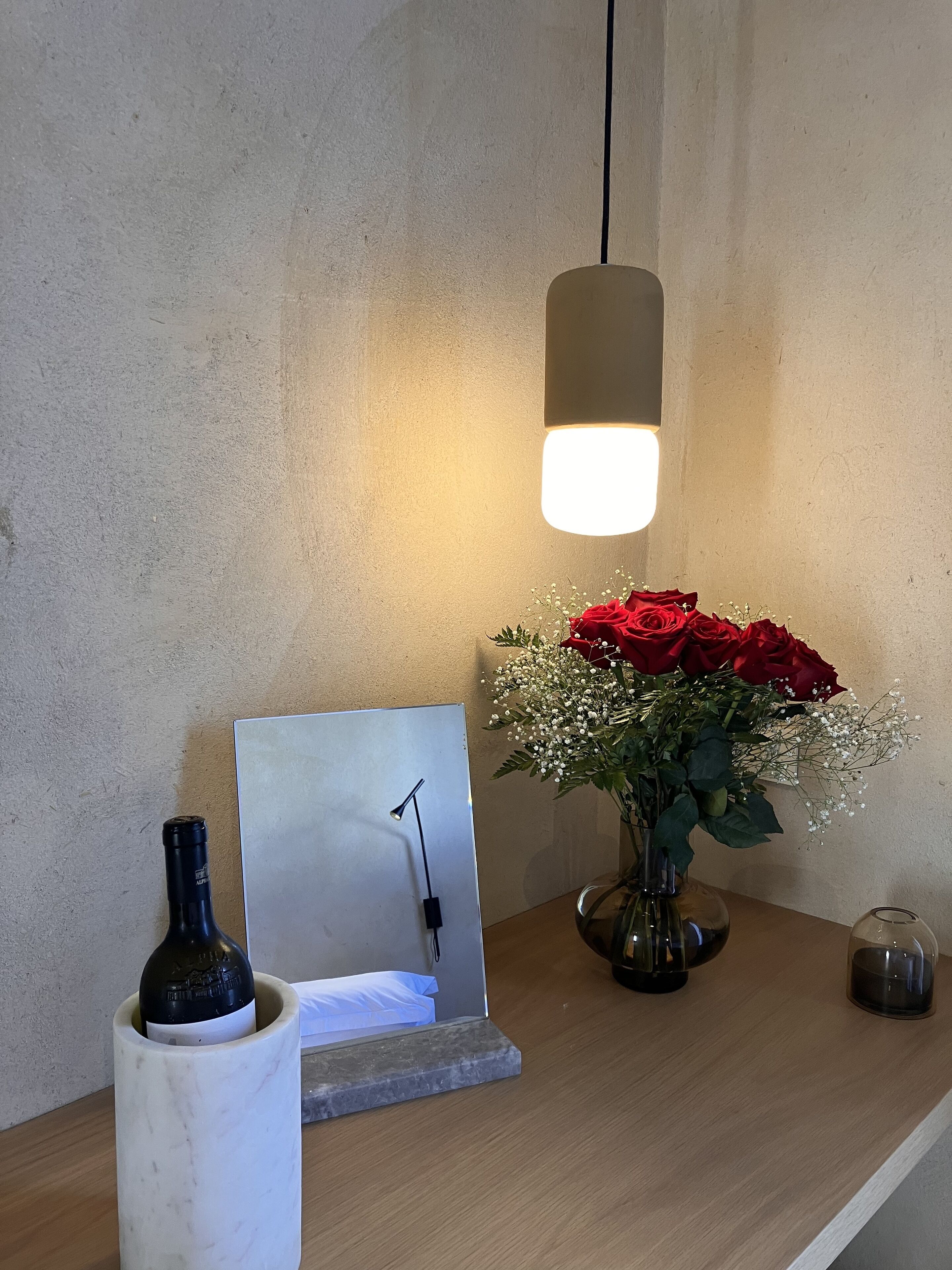 Une étagère en bois sur laquelle se trouvent une bouteille de vin, un tableau encadré, un vase de roses rouges et un petit récipient en verre.