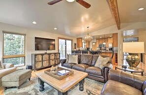 A spacious living room with a leather sofa, a coffee table, and a television. There is a kitchen in the background with wooden cabinets and a large window. - Luxury End Unit Townhome - Easy Access to Slopes - Views/Huge Deck (Durango)