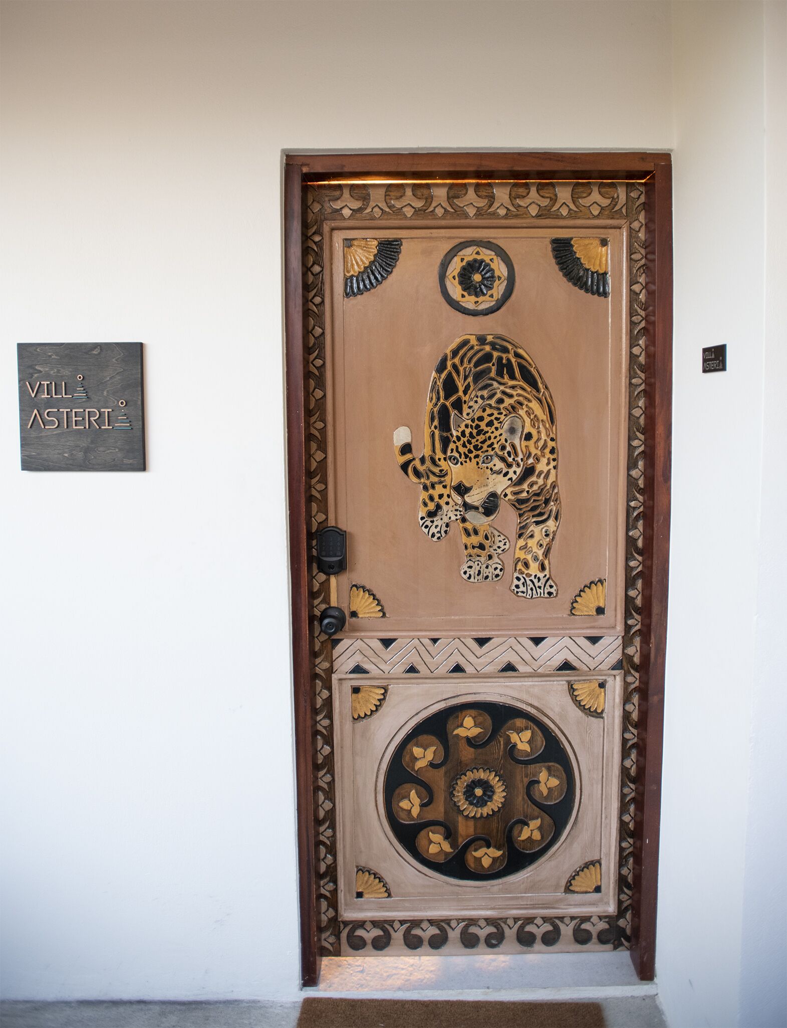 A wooden door with a leopard design, a nameplate reading "Villa Asteri", and a doormat.