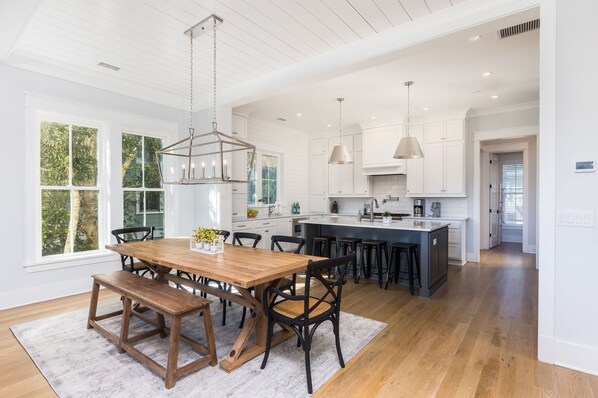 A spacious kitchen with white cabinetry, a wooden dining table, and pendant lighting.