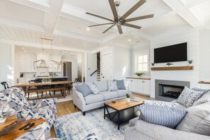 A spacious living room with a ceiling fan, a fireplace, and a large TV mounted above it.