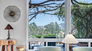 Ein gemütliches Zimmer mit großem Fenster, einem rustikalen Holztisch, zwei Stühlen und einer Lampe.