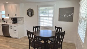 A modern kitchen with white cabinetry, a round dining table with four chairs, a clock, and a motivational quote on the wall.