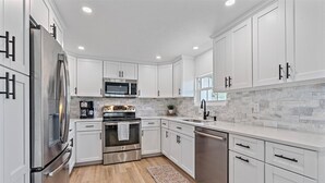 A modern kitchen with white cabinets, stainless steel appliances, and a stone backsplash.