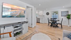 A modern kitchen with white cabinets, a dining area with a round table and chairs, and a large painting on the wall.