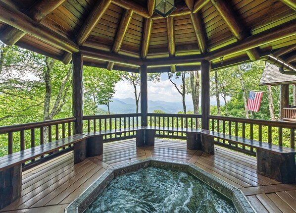 A wooden gazebo with a hot tub, surrounded by lush greenery and a view of mountains. - 4BR / 4 1/2 BA,  Covered deck with Hot-tub overlooking the mountains (Maggie Valley)