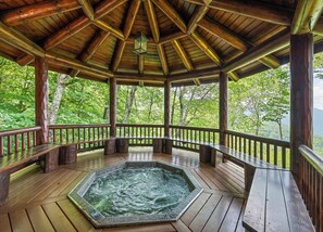 A wooden gazebo with a hot tub, benches, and a view of lush greenery. - 4BR / 4 1/2 BA,  Covered deck with Hot-tub overlooking the mountains (Maggie Valley)