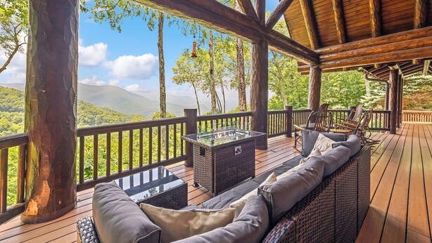 A wooden deck with a glass-top table and wicker sofa, overlooking a mountainous landscape. - 4BR / 4 1/2 BA,  Covered deck with Hot-tub overlooking the mountains (Maggie Valley)
