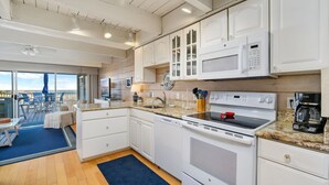 A modern kitchen with white cabinetry, a built-in microwave, a stove, and a coffee maker. - Beach Walk II 6 by Seaside Vacations & Sales (Ocean City)