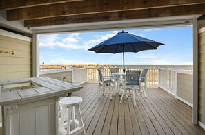 Une terrasse en bois avec une balustrade blanche, une table avec des chaises et un parasol bleu.