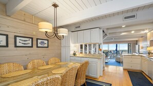 A spacious kitchen with white cabinets, a dining area with wicker chairs, and a view to the outside. - Beach Walk II 6 by Seaside Vacations & Sales (Ocean City)