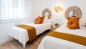A hotel room with two beds, each with white bedding and mustard-colored throw pillows. There are wall-mounted mirrors and a small potted plant on the nightstand. - SibsSanlucar- Maritimo-1ª beach line- cozy- terrace (Sanlúcar de Barrameda)