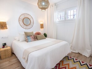 Une chambre à coucher bien aménagée, avec un grand lit, un miroir rond, des appliques murales et une fenêtre avec des rideaux.