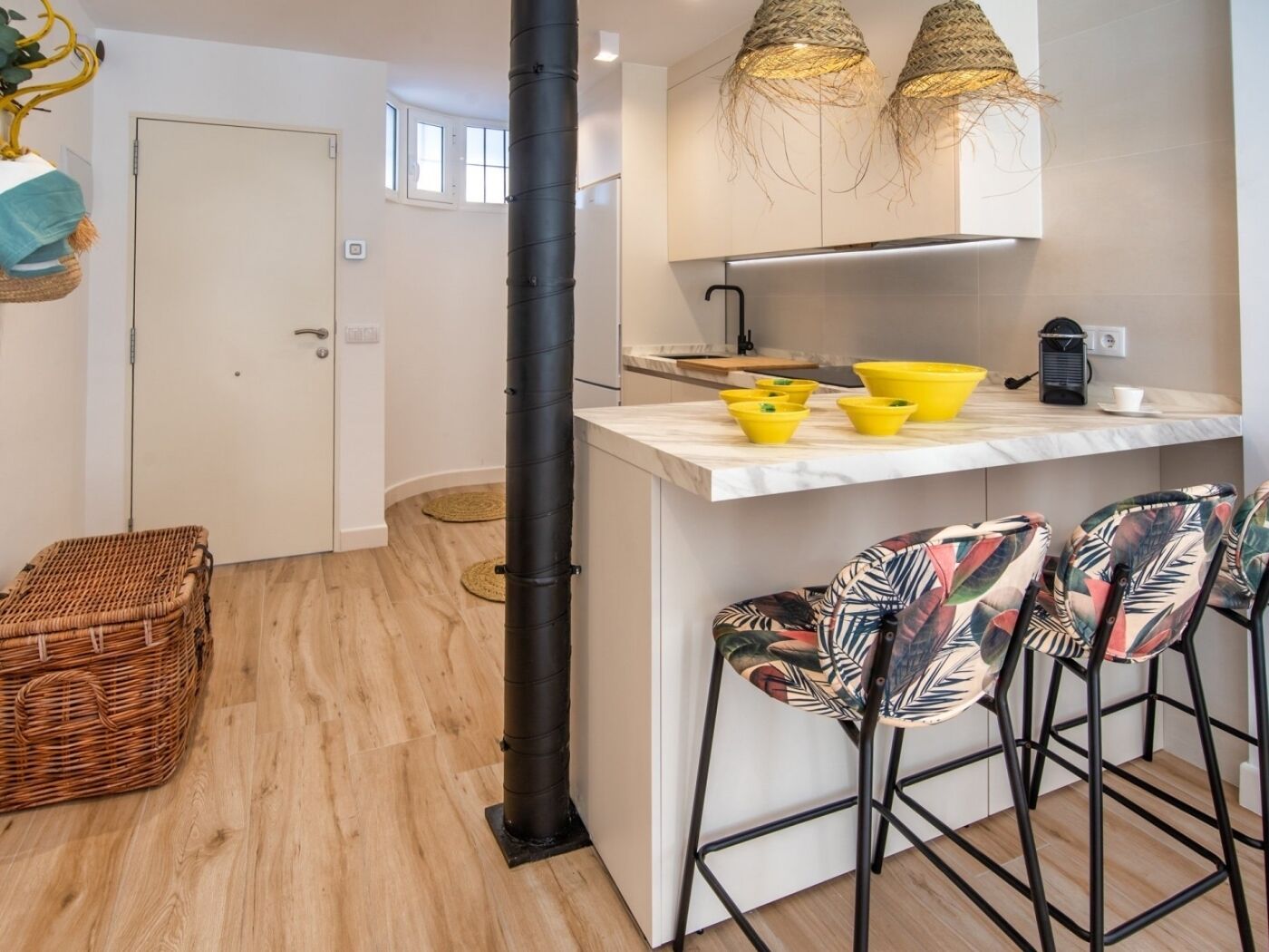 Una cocina moderna con una isla central, taburetes de bar y una lámpara colgante.