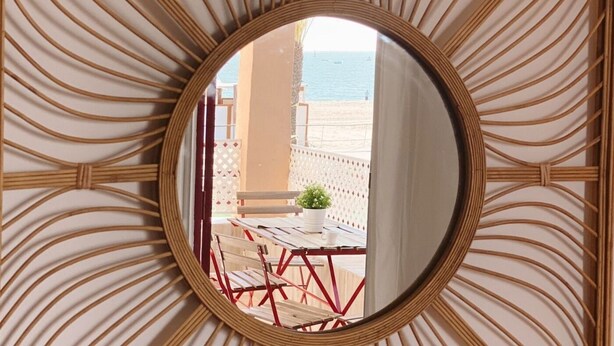 A circular mirror with a decorative frame, reflecting a balcony with red chairs and a potted plant. - SibsSanlucar- Maritimo-1ª beach line- cozy- terrace (Sanlúcar de Barrameda)