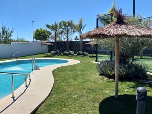 Una piscina de borde curvo, rodeada de césped cuidado y palmeras.