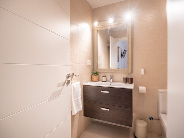 Un baño moderno con un espejo grande, un mueble de tocador de madera oscura, una toalla blanca y un inodoro.