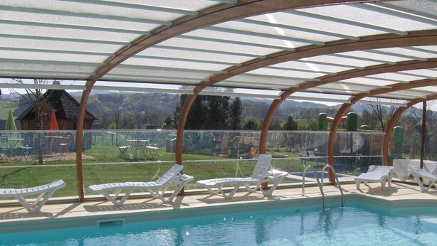 Ett poolområde med kristallklart blått vatten, vita solstolar och en träpergola som ger skugga.