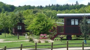 En rustik träbyggnad med en överbyggd veranda, omgiven av frodig grönska och en skogbeklädd sluttning.