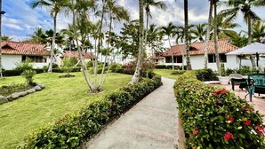 A pathway leading to a row of white buildings with red-tiled roofs, surrounded by palm trees and well-maintained gardens. - ON THE CARIBBEAN SEA - CRYSTAL APARTMENT (Boca Chica)