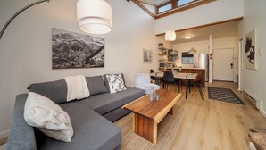 A modern living room with a grey sectional sofa, a wooden coffee table, and a mountain landscape painting on the wall. - Beaver Village Unit #0332 Remodeled 1 Bedroom vaulted ceiling & private deck (Winter Park)