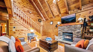 A cozy log cabin interior with a stone fireplace, wooden staircase, and comfortable seating areas. - PROMO 10% WEEKLY DISCOUNT September Special,Hot tub Pool table, Arcades WIFI-Pet (Sevierville)
