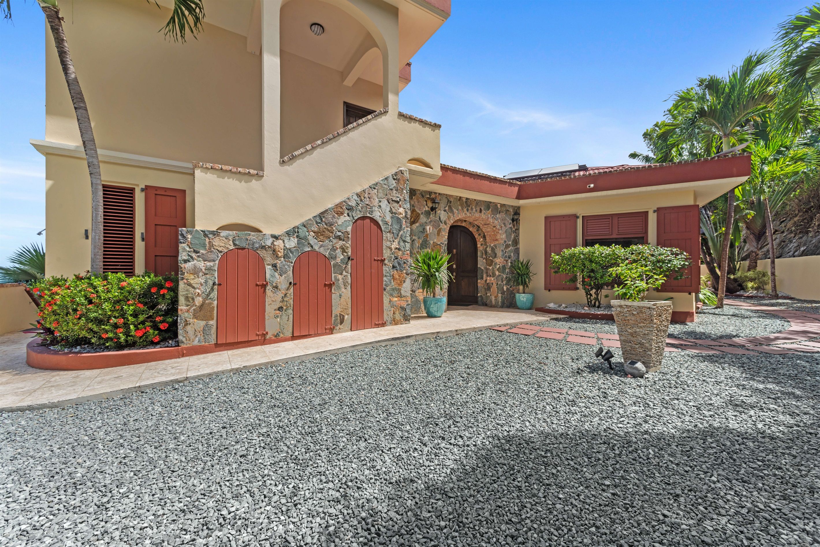 A two-story building with a stone facade, red doors, and a gravel driveway.