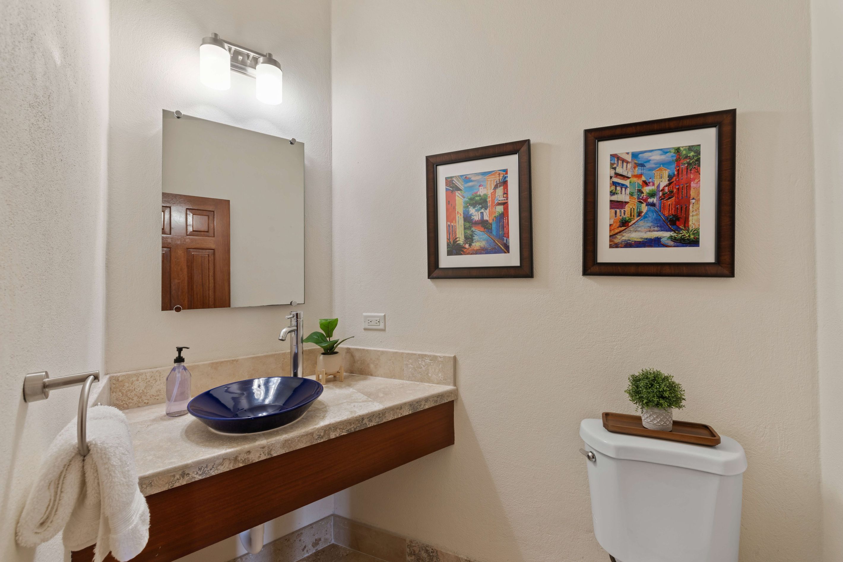 A bathroom with a sink, mirror, and two framed paintings on the wall.