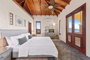 A bedroom with a bed, a nightstand, a dresser, a ceiling fan, and a large window with shutters.