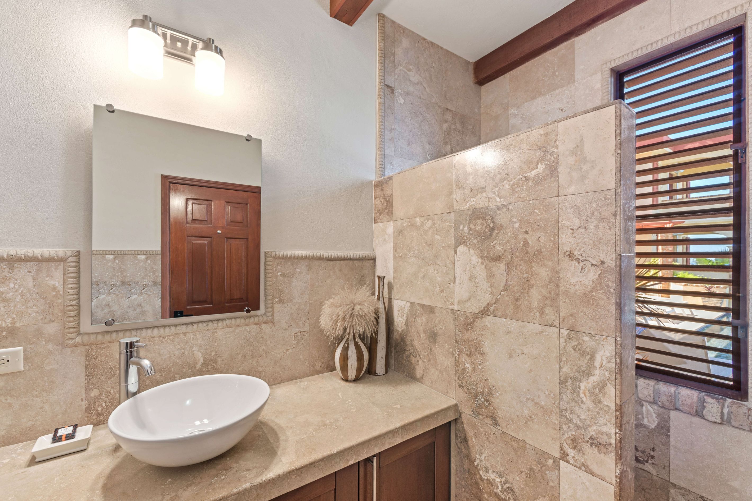 A bathroom with a white vessel sink, a mirror, and a wooden door.