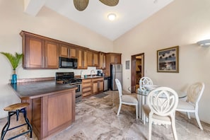 A kitchen with wooden cabinets, a gas stove, a microwave, a refrigerator, and a dining area with white chairs.