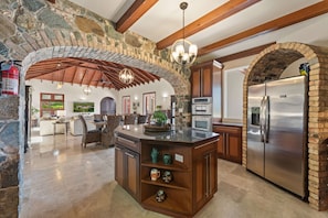 A spacious kitchen with a stone arch, wooden beams, and modern appliances.