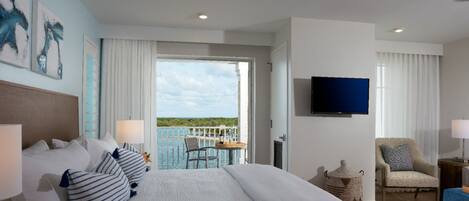 Une chambre d’hôtel avec un grand lit, une télévision, un balcon donnant sur la mer et un fauteuil.