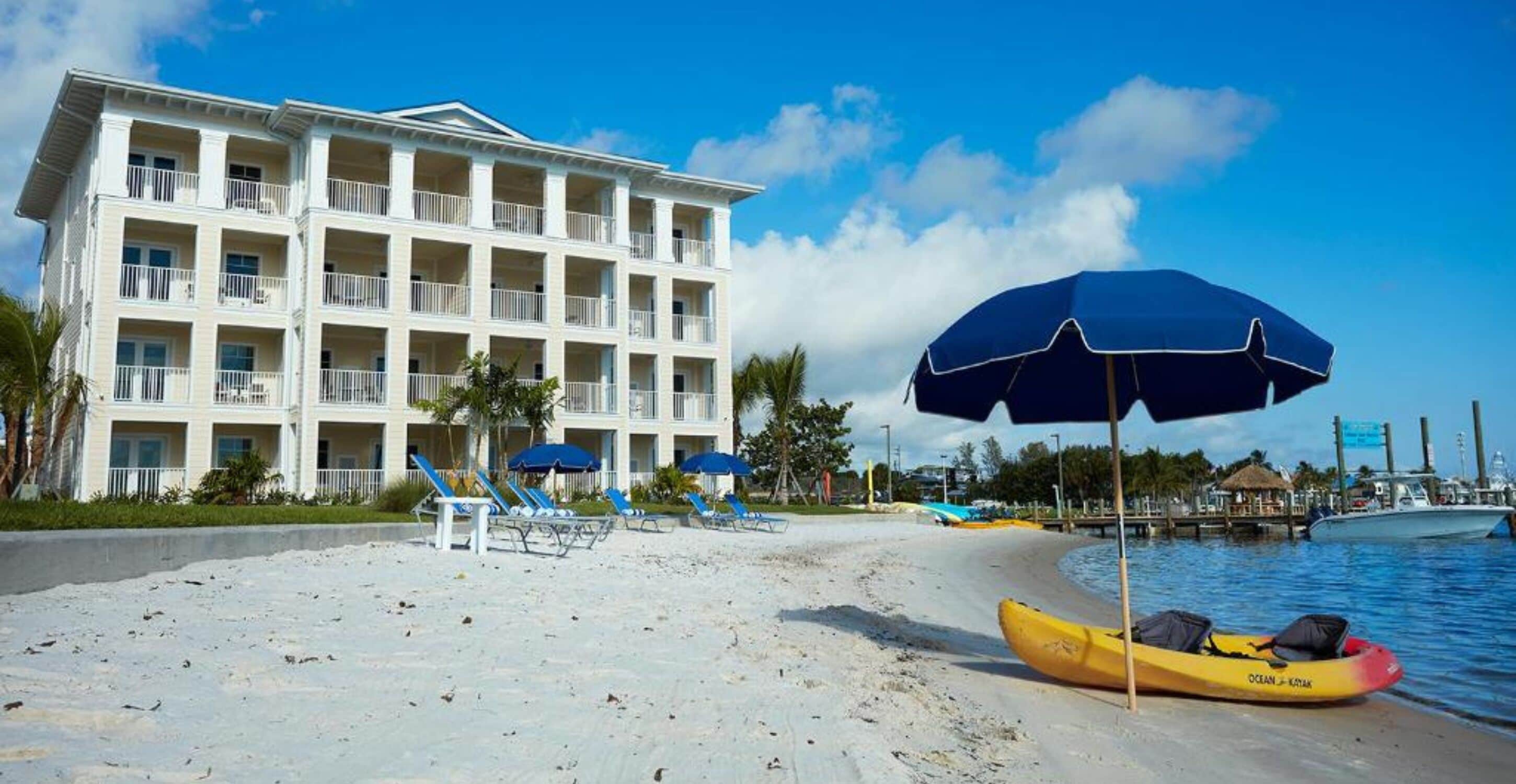 Un hôtel situé en bord de mer, doté de nombreux balcons, d’une plage de sable et d’un kayak à proximité de l’eau.