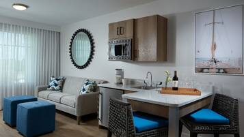 A modern living room with a sofa, ottomans, a dining table with chairs, a kitchen area with a microwave, and a large mirror.