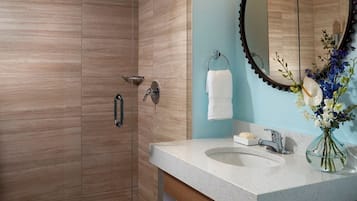 A modern bathroom with a glass-enclosed shower, a marble-tiled floor, a sink with a soap dish, and a mirror with a decorative frame.